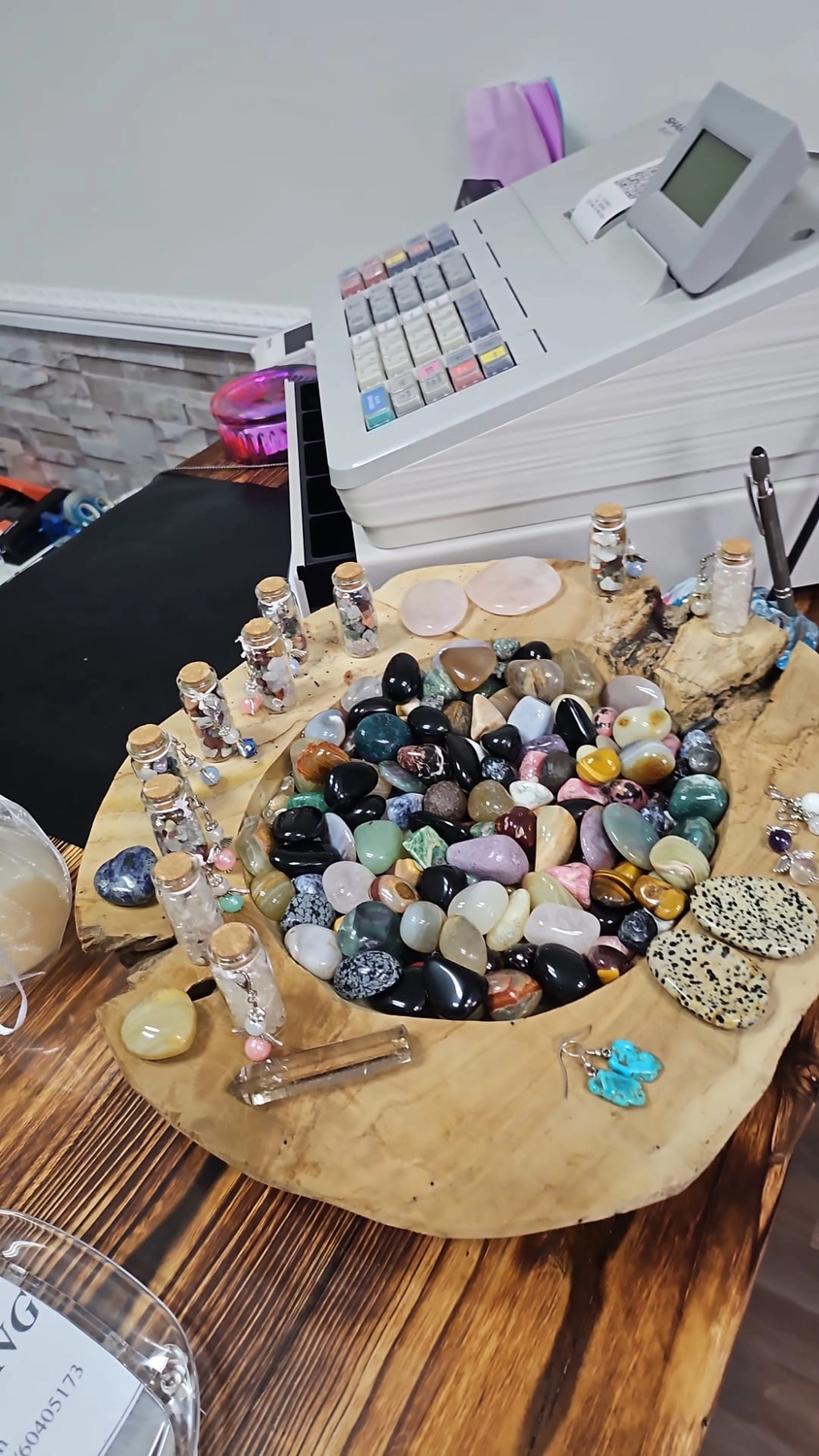Jassis Schatzkiste – Handarbeit und Esoterik – eine Vielzahl polierter und roher Kristalle, darunter etwas, das wie eine große Schale mit Trommelsteinen aussieht, und kleinere Fläschchen mit Chips.