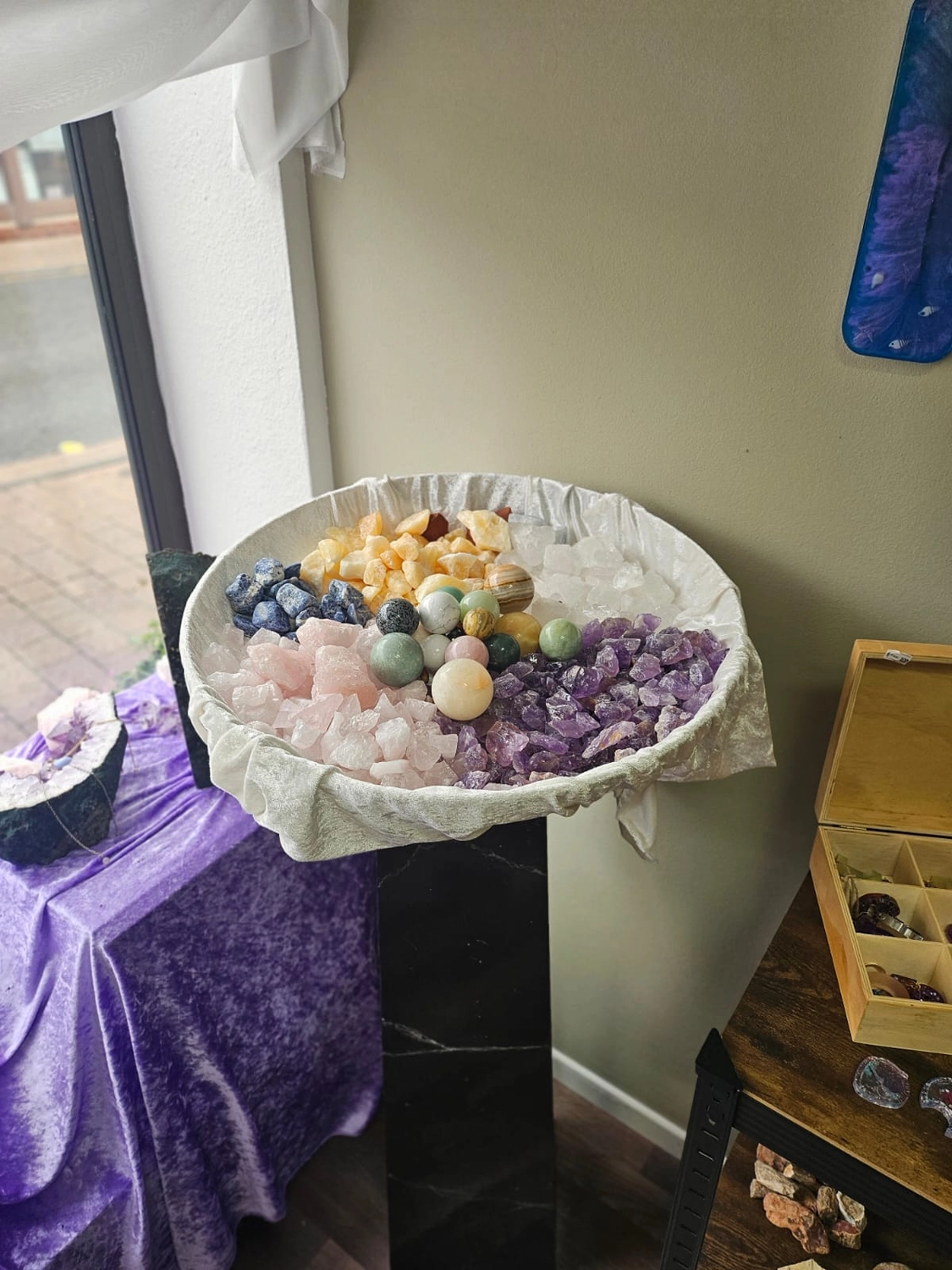 Jassis Schatzkiste – Handarbeit und Esoterik – eine Vielzahl polierter und roher Kristalle, darunter etwas, das wie eine große Schale mit Trommelsteinen aussieht, und kleinere Fläschchen mit Chips.