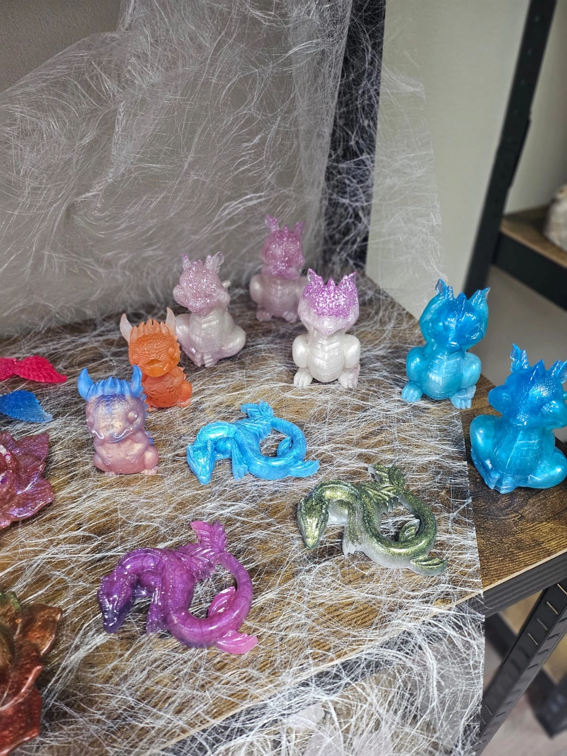 Jassi´s Schatzkiste – Handarbeit und Esoterik – eine Sammlung kleiner, bunter Figuren von Babydrachen, die wahrscheinlich aus Epoxidharz mithilfe von Silikonformen hergestellt werden.