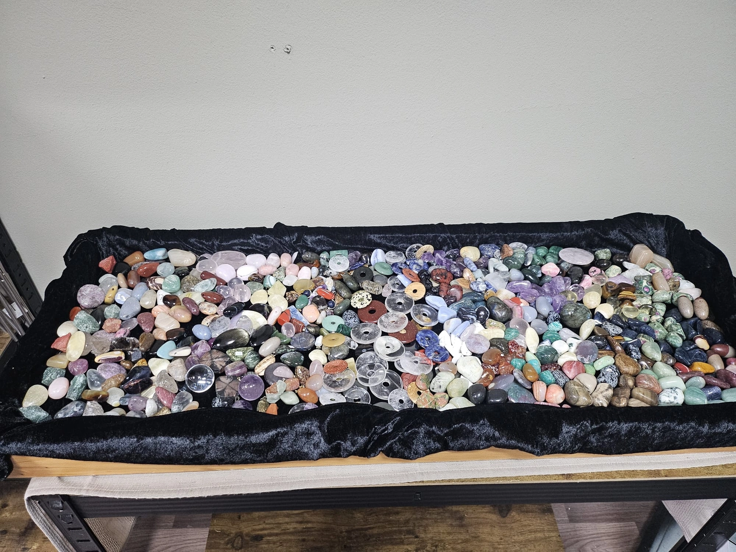 Jassis Schatzkiste – Handarbeit und Esoterik – eine Vielzahl polierter und roher Kristalle, darunter etwas, das wie eine große Schale mit Trommelsteinen aussieht, und kleinere Fläschchen mit Chips.